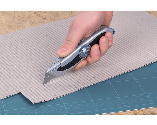 Eine Hand schneidet mit einem Universalmesser Pappe.