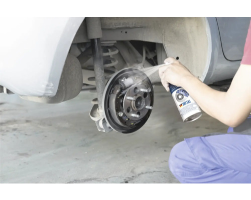 Eine Person reinigt eine offene Trommelbremse eines Autos mit Bremsenreiniger.