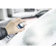 Eine Hand hält eine Sprühdose Enteiser und sprüht auf eine vereiste Windschutzscheibe.