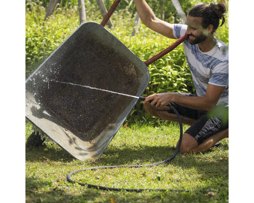 Ein Mann reinigt eine Schubkarre mit einem Gartenschlauch im Garten.