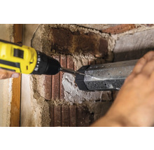 Eine Person befestigt eine Metallkonstruktion mit einem Akkuschrauber an einer Ziegelwand.