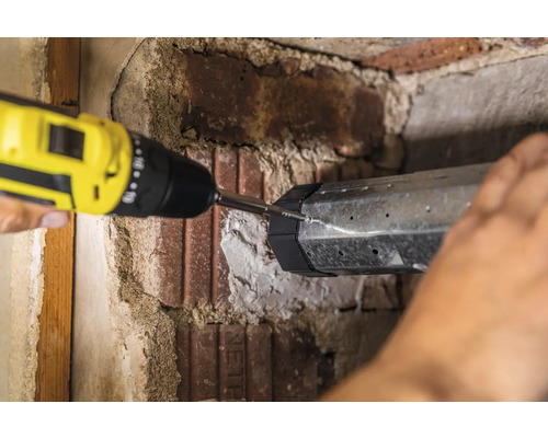 Eine Person befestigt eine Metallkonstruktion mit einem Akkuschrauber an einer Ziegelwand.