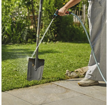 Eine Person reinigt eine Gartenschaufel mit einem Gartenschlauch im Freien.