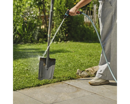 Eine Person reinigt eine Gartenschaufel mit einem Gartenschlauch im Freien.