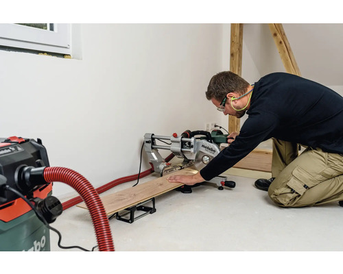 Ein Handwerker sägt ein Holzbrett mit einer Metabo Kappsäge in einer hellen Werkstatt.