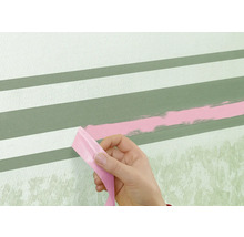 Eine Person entfernt Klebeband von einer Wand mit gemalten Streifen.