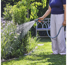 Eine Person bewässert mit einem Gartenschlauch Pflanzen im Garten.