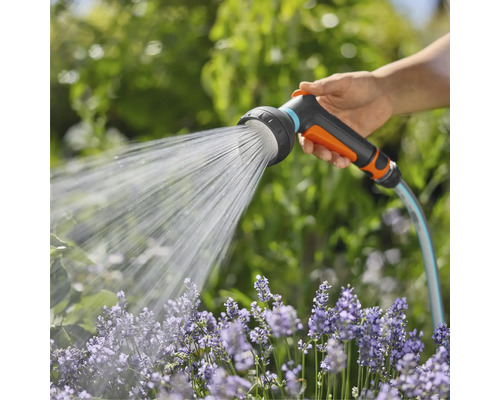 Eine Hand hält einen Gartenschlauch mit Brausekopf, der Wasser auf Blumen sprüht.