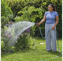 Frau bewässert Pflanzen mit Gartenschlauch im Garten.