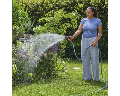 Frau bewässert Pflanzen mit Gartenschlauch im Garten.