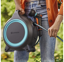 Eine Person hält eine Gardena Schlauchbox mit Gartenschlauch und Spritze.