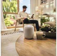 Intelligenter Lautsprecher auf einem runden Holztisch in einem Wohnzimmer