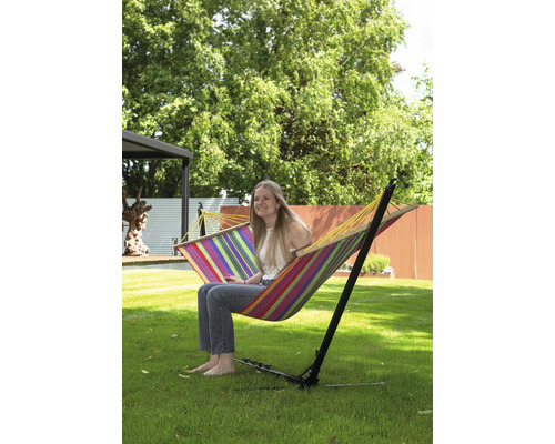 Frau sitzt in einer gestreiften Hängematte mit Gestell im Garten.