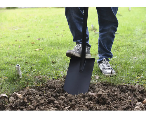Eine Person benutzt einen Spaten im Garten, um Erde umzugraben.