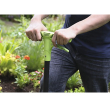 Person benutzt einen Unkrautstecher im Garten.