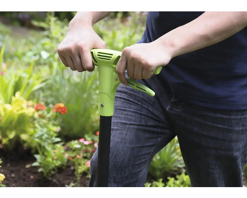 Person benutzt einen Unkrautstecher im Garten.