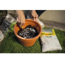 Eine Person mischt Blumenerde mit Perlit in einem Pflanzgefäß. Eine Packung Flora Gard Perlite liegt daneben.