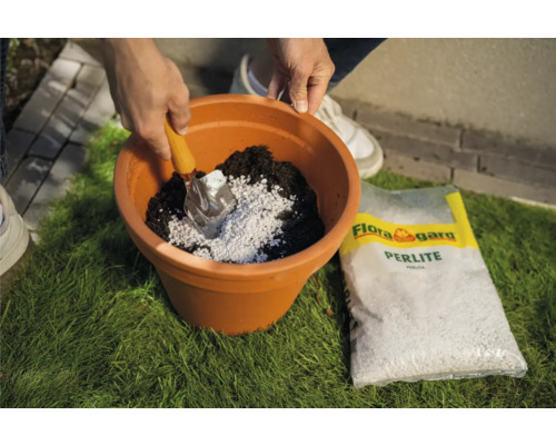 Gartenszene mit Person, die Perlite mit einer Schaufel in einen Pflanztopf mit Erde mischt, und eine Packung Flora Gard Perlite.