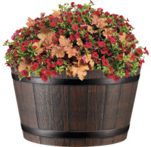 Blumenarrangement mit roten Blüten und Zierblättern in einem Holzfass