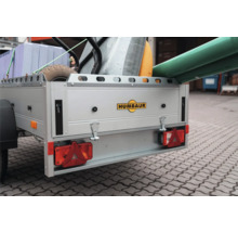 Beladener Humbaur Anhänger mit Baumaterialien wie Dämmplatten, einem Wellrohr und Rohren. Humbaur Logo auf der Heckklappe.