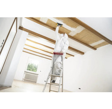 Handwerker auf einer Leiter bei Renovierungsarbeiten an einer Decke in einem hellen Raum.