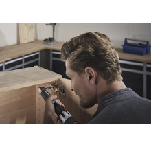 Ein Mann befestigt ein Scharnier mit einem Akku-Bohrschrauber an einem Holzschrank.