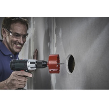 Ein Mann mit Schutzbrille bohrt mit einer Lochsäge ein Loch in eine Wand.