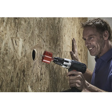 Mann bohrt mit einer Lochsäge ein Loch in eine Holzplatte.