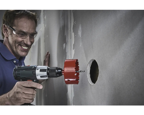 Ein Mann bohrt mit einer Lochsäge ein Loch in eine Wand.