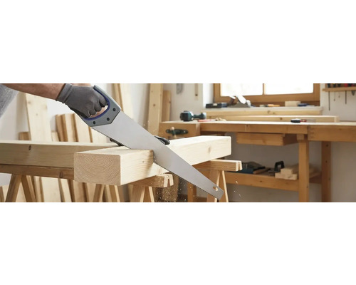 Eine Handsäge schneidet ein Holzstück auf einer Werkbank.