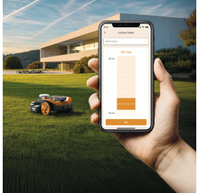 Ein Rasenmähroboter steht auf einem Rasen, während eine Hand ein Smartphone mit einer App zur Schnitthöhenverstellung hält.