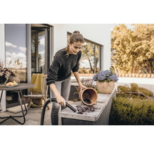 Frau reinigt Terrasse mit Staubsauger neben Blumentopf
