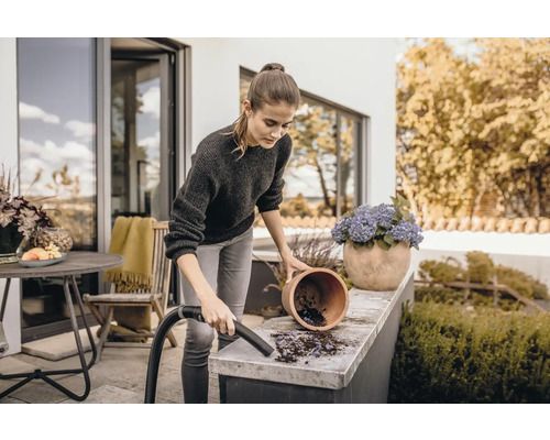 Frau reinigt Terrasse mit Staubsauger neben Blumentopf