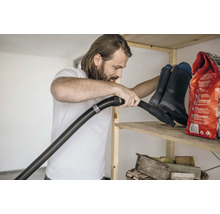 Mann saugt Regal mit Gummistiefeln und Sack ab