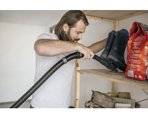 Mann saugt Regal mit Gummistiefeln und Sack ab