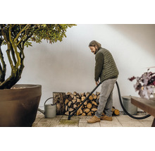 Mann reinigt Terrasse mit einem Aschesauger, im Hintergrund Holzstapel und eine Pflanze