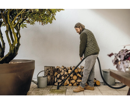 Mann reinigt Terrasse mit einem Aschesauger, im Hintergrund Holzstapel und eine Pflanze