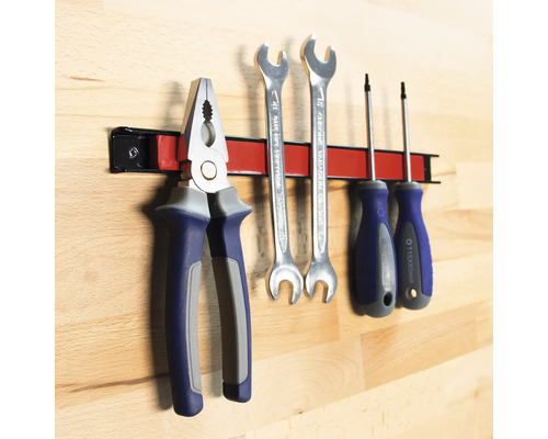 Werkzeuge wie Zange, Schraubenschlüssel und Schraubendreher an einer magnetischen Werkzeugleiste.