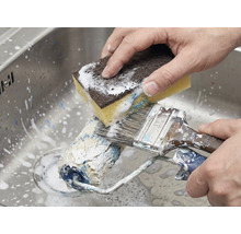 Reinigung von Farbroller und Pinsel mit einem Schwamm im Spülbecken.