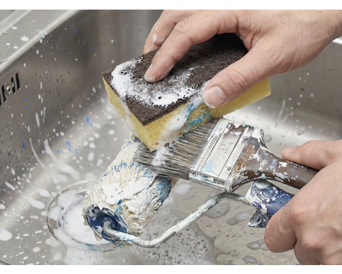 Reinigung von Farbroller und Pinsel mit einem Schwamm im Spülbecken.