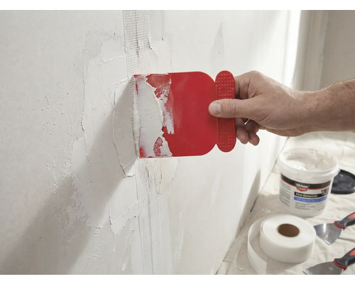 Ein Mann trägt eine rote Spachtel auf eine Wand mit Glasfaserklebeband auf