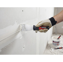 Handwerker spachtelt Wand mit Spachtel und Spachtelmasse. Rautner Logo sichtbar.