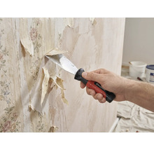 Eine Person entfernt mit einem Spachtel alte Tapeten von einer Wand.