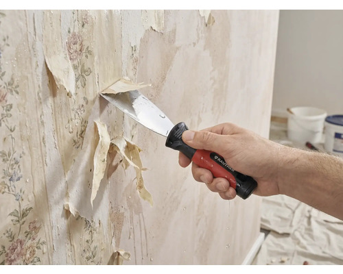 Eine Person entfernt mit einem Spachtel alte Tapeten von einer Wand.