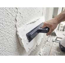 Handwerker trägt mit einer Glättkelle Putz auf eine Wand auf.