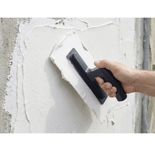 Eine Person trägt mit einer Glättkelle Putz auf eine Wand auf.