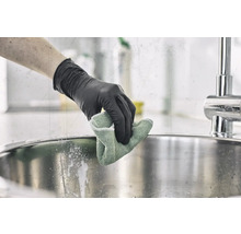 Eine Person mit Handschuhen reinigt ein Spülbecken mit einem Tuch.