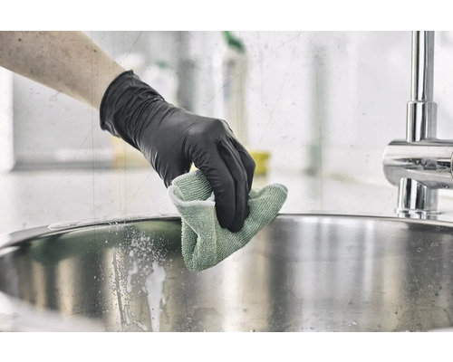 Eine Person mit Handschuhen reinigt ein Spülbecken mit einem Tuch.