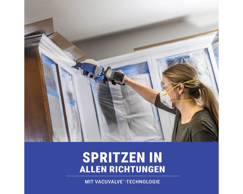 Frau sprüht mit einer Farbspritzpistole Farbe auf einen Schrank.