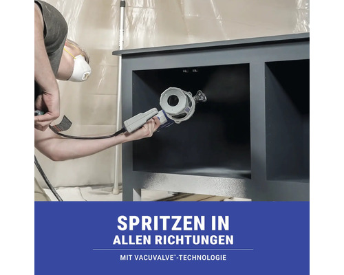 Eine Person sprüht mit einem Farbspritzgerät Farbe auf ein graues Möbelstück.